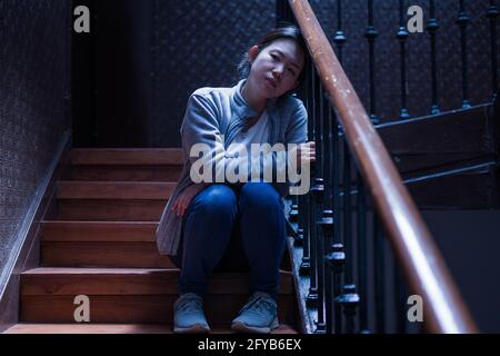 young beautiful Asian woman in pain suffering depression - dramatic indoors portrait on staircase of sad and depressed Japanese girl as victim of bull