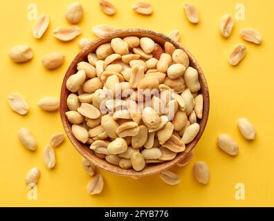 wooden bowl of roasted salted peanuts on yellow background, top view Stock Photo