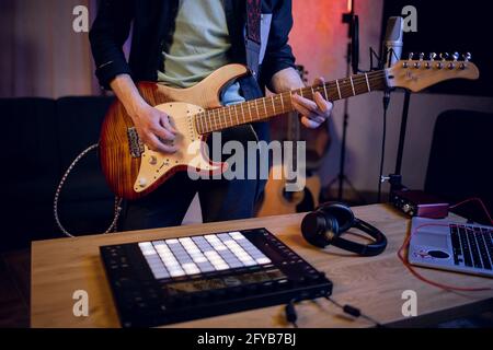 Close up of male musician playing guitar and using dj controller for mixing sounds. Man with modern equipments creating new music at studio. Stock Photo