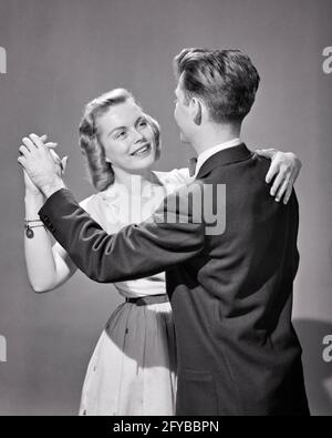 1950s SMILING YOUNG TEENAGE COUPLE MAN WOMAN DANCING ARM IN ARM - d3110 DEB001 HARS PAIR ROMANCE SUBURBAN URBAN RELATIONSHIP DANCERS OLD TIME NOSTALGIA OLD FASHION 1 JUVENILE COMMUNICATION YOUNG ADULT STRONG JOY LIFESTYLE FEMALES STUDIO SHOT COPY SPACE FRIENDSHIP HALF-LENGTH PERSONS CARING MALES TEENAGE GIRL TEENAGE BOY ENTERTAINMENT B&W DATING SCHOOLS DREAMS HAPPINESS UNIVERSITIES ARM IN ARM ATTRACTION HIGH SCHOOL HIGH SCHOOLS HIGHER EDUCATION CONNECTION COURTSHIP CONCEPTUAL STYLISH TEENAGED YOUNG LOVE COLLEGES DEB001 PERSONAL ATTACHMENT POSSIBILITY AFFECTION EMOTION JUVENILES SOCIAL ACTIVITY Stock Photo