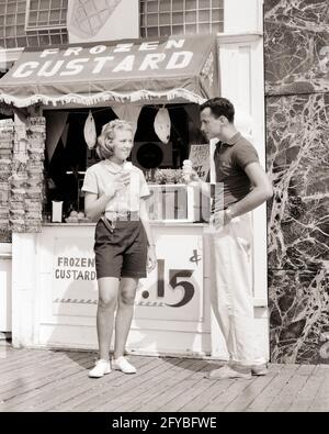 1950s 1960s DATING TEENAGE COUPLE EATING FROZEN CUSTARD CONES STANDING IN FRONT OF SEASHORE BOARDWALK STAND NEW JERSEY USA - f7703 HAR001 HARS COPY SPACE FRIENDSHIP FULL-LENGTH BOYFRIEND CARING MALES TEENAGE GIRL TEENAGE BOY BOARDWALK B&W SUMMERTIME DATING GIRLFRIEND SHORE HAPPINESS ADVENTURE LEISURE EXTERIOR ATTRACTION CONES NJ CONNECTION COURTSHIP STYLISH ICE CREAM POSSIBILITY CUSTARD JUVENILES SEASON SOCIAL ACTIVITY TOGETHERNESS BLACK AND WHITE CAUCASIAN ETHNICITY COURTING HAR001 OLD FASHIONED Stock Photo