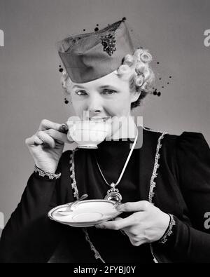 1930s 1940s ELEGANT MID-ADULT WOMAN LOOKING AT CAMERA DRINKING FROM CHINA TEA CUP WEARING HAT JEWELRY AT SOCIAL SOCIETY FUNCTION - f9529 HAR001 HARS HOME LIFE LUXURY COPY SPACE HALF-LENGTH INSPIRATION ENTERTAINMENT CONFIDENCE B&W EYE CONTACT HAPPINESS WELLNESS LEISURE STRENGTH CHOICE EXCITEMENT POWERFUL SOCIETY PRIDE AT OPPORTUNITY AUTHORITY OCCUPATIONS UPSCALE CONNECTION CONCEPTUAL AFFLUENT STYLISH FUNCTION MID-ADULT MID-ADULT WOMAN RELAXATION SIPPING WELL-TO-DO BLACK AND WHITE CAUCASIAN ETHNICITY HAR001 OLD FASHIONED SAUCER SOCIALITE Stock Photo