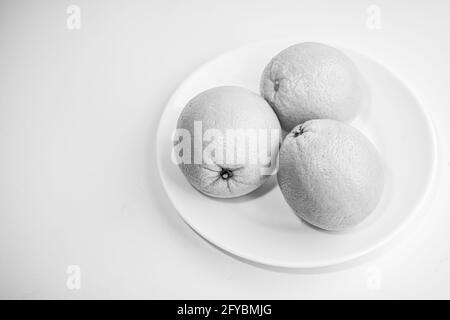 Three oranges in a plate on a white background. Black and white photo. Still life. Selective focus. Stock Photo