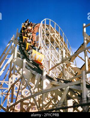1970s CARS ON WOODEN SUPPORTED TRACK ROLLER COASTER THRILL RIDE AT AMUSEMENT PARK ON DOWNWARD CURVE - kf11555 HAR001 HARS THRILL HEAD AND SHOULDERS EXTERIOR LOW ANGLE RECREATION CONCEPTUAL TEENAGED DOWNWARD RIDES SUPPORTED AMUSEMENT PARK CURVE HAR001 OLD FASHIONED ROLLER COASTER THRILLING Stock Photo