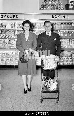 1940s MAN AND WOMAN COUPLE SHOPPING IN GROCERY STORE MAN PUSHING GROCERY CART - s11552 HAR001 HARS EXPRESSION OLD TIME BUSY NOSTALGIA OLD FASHION 1 SILLY FACIAL YOUNG ADULT COMIC TEAMWORK PLEASED JOY LIFESTYLE FEMALES MARRIED SPOUSE HUSBANDS COPY SPACE FULL-LENGTH LADIES PERSONS SHOPS MALES EXPRESSIONS B&W PARTNER SHOPPER EYE CONTACT SHOPPERS SUIT AND TIE HUMOROUS CHEERFUL DISCOVERY AND CHOICE COMICAL SMILES STORES CONCEPTUAL COMEDY JOYFUL STYLISH POCKETBOOK COMMERCE TOGETHERNESS WIVES YOUNG ADULT MAN YOUNG ADULT WOMAN BLACK AND WHITE BUSINESSES CAUCASIAN ETHNICITY HAR001 OLD FASHIONED Stock Photo