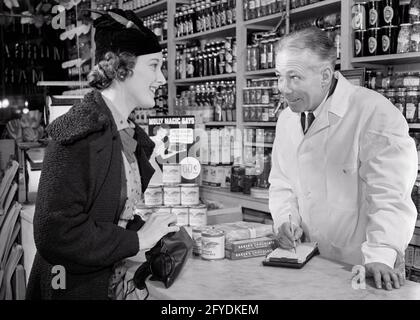 1930s FASHIONABLE SMILING WOMAN AT COUNTER OF GROCERY STORE GIVING ORDER TO MAN A GROCER LISTENING AND WRITING IN HIS SALES PAD - s10673 HAR001 HARS URBAN OLD TIME BUSY NOSTALGIA OLD FASHION 1 GIVING STYLE WELCOME PAD COMMUNICATION YOUNG ADULT INFORMATION FASHIONABLE PLEASED JOY LIFESTYLE CLERK FEMALES HOME LIFE COPY SPACE FRIENDSHIP HALF-LENGTH LADIES PERSONS SHOPS MALES ORDER MIDDLE-AGED B&W MIDDLE-AGED MAN HAPPINESS CHEERFUL HIS STYLES CUSTOMER SERVICE AND GROCER LABOR EMPLOYMENT OCCUPATIONS SMILES STORES FRIENDLY JOYFUL STYLISH EMPLOYEE COMMERCE COOPERATION FASHIONS YOUNG ADULT WOMAN Stock Photo