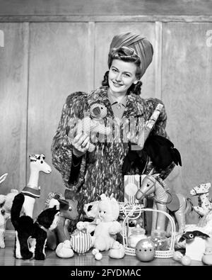 1940s FASHIONABLE WOMAN CHRISTMAS SHOPPING IN TURBAN STYLE HAT FAUX FUR COAT LOOKING AT CAMERA HOLDING TOY AND WRAPPED PACKAGE - s9799 HAR001 HARS FASHIONABLE PLEASED JOY LIFESTYLE FEMALES STUDIO SHOT STUFFED COPY SPACE HALF-LENGTH LADIES PERSONS PACKAGE CONFIDENCE B&W SHOPPER EYE CONTACT BRUNETTE SHOPPERS HAPPINESS CHEERFUL STYLES MERRY OPPORTUNITY SMILES DECEMBER DECEMBER 25 FAUX JOYFUL STYLISH TURBAN FASHIONS JOYOUS MID-ADULT MID-ADULT WOMAN BLACK AND WHITE CAUCASIAN ETHNICITY HAR001 OLD FASHIONED Stock Photo