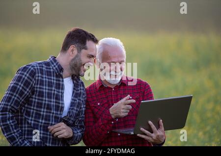 Farmers using laptop outside for agriculture.. Two men standing in field  pointing showing smiling at screen. Stock Photo