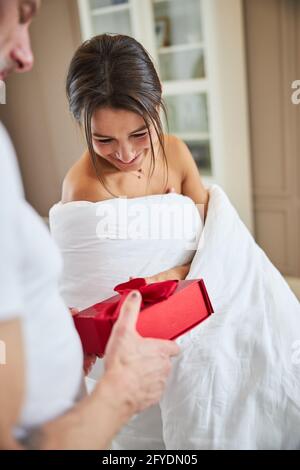Funny gorgeous female covered in quilt with gift in arms in cozy apartment Stock Photo
