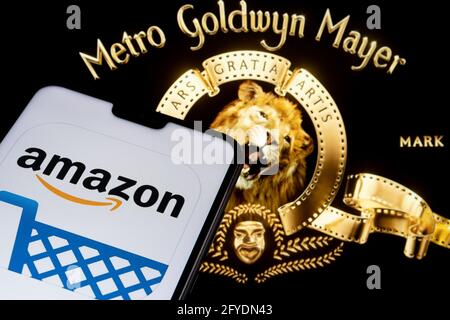 Amazon app logo seen on the smartphone and blurred Metro Goldwyn Mayer logo on the laptop. Stafford, United Kingdom, May 27, 2021. Stock Photo
