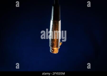 Closeup of Dangling Worn out and Scratched Male XLR Connector isolated on Blue Background with Orange Lighting Stock Photo