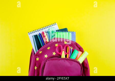 Red backpack with different colorful stationery on yellow background. Back to school concept. Top view, copy space Stock Photo