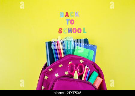 Red backpack with different colorful stationery on yellow background. Back to school concept. Top view, copy space Stock Photo