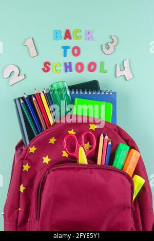 Red backpack with different colorful stationery on pastel green background. Back to school concept. Top view, copy space Stock Photo
