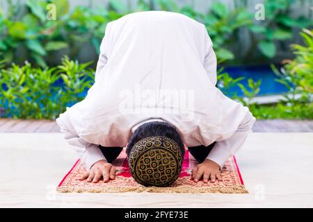 Asian Muslim man praying on carpet wearing traditional dress Stock Photo