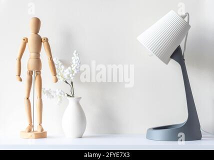 Interior of living room. Wooden mannequin, vase with decor plant, lamp on white wooden desk, mockup, minimal composition, space for text Stock Photo