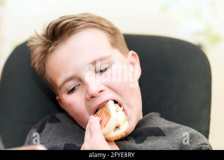 A Hungry boy eating a hot dog at home kid eats a hot-dog sandwich.Indoors shot.Closeup. Stock Photo