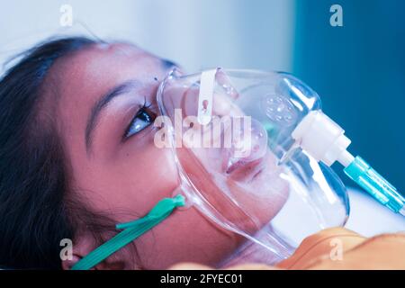 Close up shot of little girl kid breathing on ventilator oxygen mask at hospital due to coronavirus covid-19 breath shortness or dyspnea - concept of Stock Photo