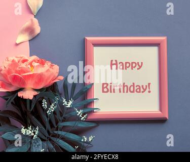Happy birthday card with peony flower and petals. Single flower and white frame on pink and dark grey layered grey paper background. Creative flat lay Stock Photo