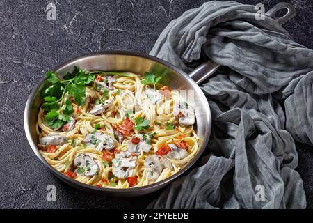 Italian pasta with cremini mushroom sauce of heavy cream and parmesan  cheese with crispy bacon and fresh parsley served on a metal skillet on a dark