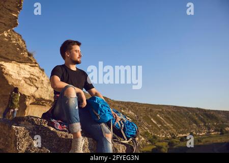 Dreamy young hiker man sitting on the edge of the mountain and looking into the distance. Stock Photo