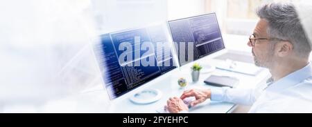 Programmer In Office Working On Multiple Computer Monitor Screens Stock Photo