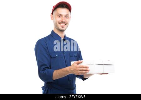 Horizontal medium portrait of handsome young adult Caucasian delivery man wearing blue uniform holding box, white background Stock Photo