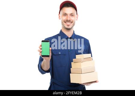 Horizontal medium portrait of handsome young adult Caucasian delivery man wearing blue uniform holding boxes using smartphone, white background Stock Photo