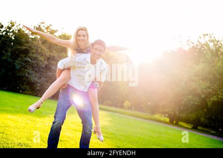 Man carrying girl piggyback in summer in backlit sunset scene Stock Photo