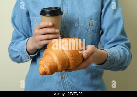 Woman holds paper cup and croissant on beige background Stock Photo