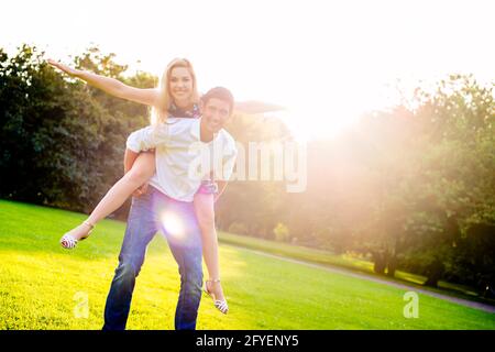 Man carrying girl piggyback in summer in backlit sunset scene Stock Photo