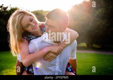 Man carrying girl piggyback in summer in backlit sunset scene Stock Photo