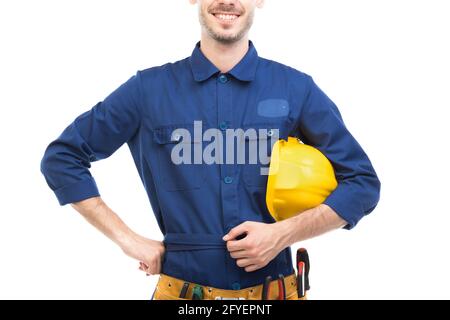 Horizontal medium portrait of successful handsome young adult Caucasian construction engineer wearing blue uniform holding hardhat, white background Stock Photo