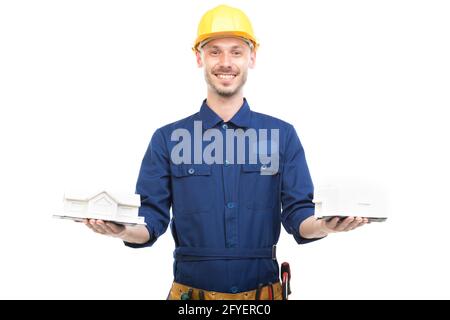 Horizontal medium portrait of modern handsome young adult Caucasian engineer wearing blue uniform holding two house models, white background Stock Photo