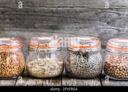 Healthy vegan food, seeds and grains in jars on rustic table, chickpeas, peas, sunflower seed, oatmeal Stock Photo