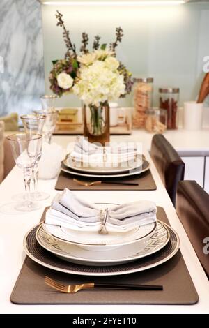 tableware for dinner consis of three size plates with two wine glasses, knife and fork, two napkins put on the counter in kitchen Stock Photo