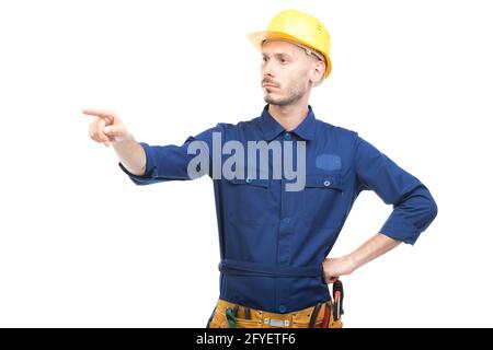 Horizontal medium portrait of modern handsome young adult Caucasian engineer wearing blue uniform pointing finger at something, white background Stock Photo