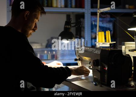 Hipster designer man sew at sewing machine. Creative work in tailoring studio or atelier concept Stock Photo