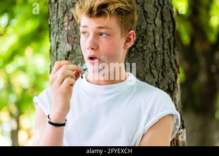 Portrait of young boy smoking in front of tree trunk Stock Photo