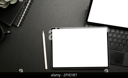 Top view of dark workspace with two tablets, accessories, stationery and copy space, clipping path Stock Photo