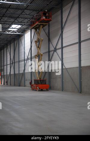 VENLO, NETHERLANDS - May 10, 2017: A scissor lift in an empty warehouse. On the platform near the roof is an engineer fixing the roof. Stock Photo