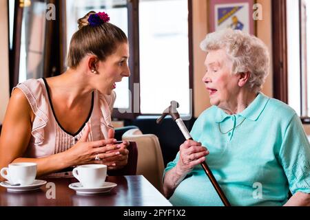 Grandmother and granddaughter having argument in cafe, the senior woman in threatening with her crutch Stock Photo