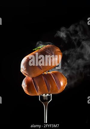 Hot juicy meat sausages on a fork, covered in smoke on a black background. Tasty food. Copy space. Stock Photo