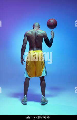 Sportive athletic african-american male basketball player posing in neon light on blue background. Rear view Stock Photo