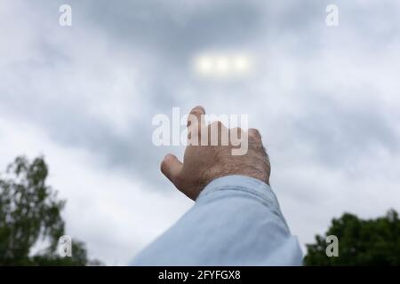 Man pointing finger at the strange lights in the sky, three light orbs among the clouds, UFO concept Stock Photo