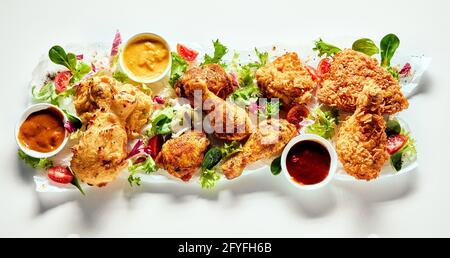Top view of appetizing fried chicken legs in crispy breading served with tomatoes and salad leaves and different sauces Stock Photo