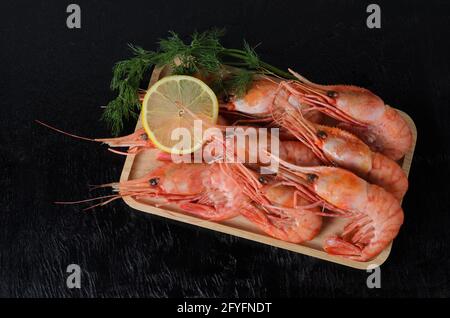 Boiled shrimps in a shell with dill and lemon in a wooden bowl on a dark wooden background. Selective focus. Stock Photo