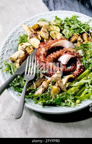 Seafood salad. Coocked grilled tentacles of octopus, sardines and mussels on blue ceramic plate served with arugula salad, zucchini and asparagus over Stock Photo