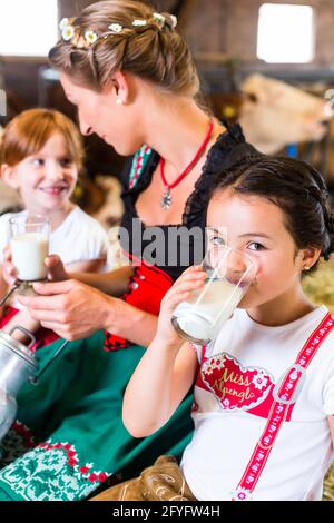 Bavarian mother sitting with children in cowhouse on hay bale drinking fresh milk Stock Photo