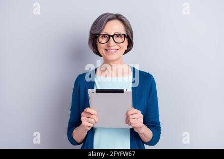Portrait of nice smart cheerful gray haired woman holding in hands using tablet web isolated over grey pastel color background Stock Photo